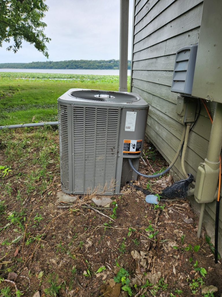 An old, worn outdoor AC condenser unit beside a house, showing rust and wear typical of a system nearing the end of its service life.
