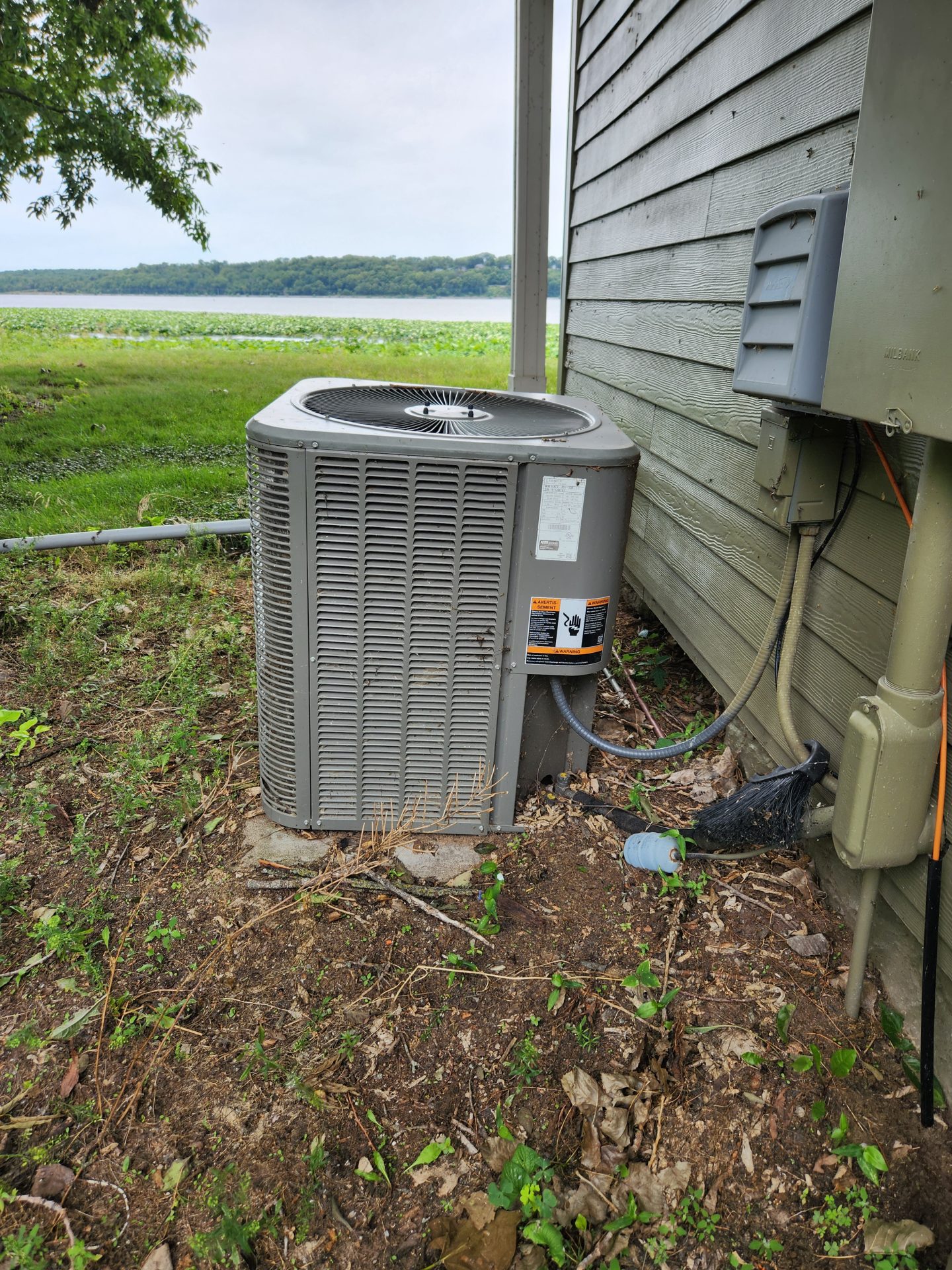 An old, worn outdoor AC condenser unit beside a house, showing rust and wear typical of a system nearing the end of its service life.